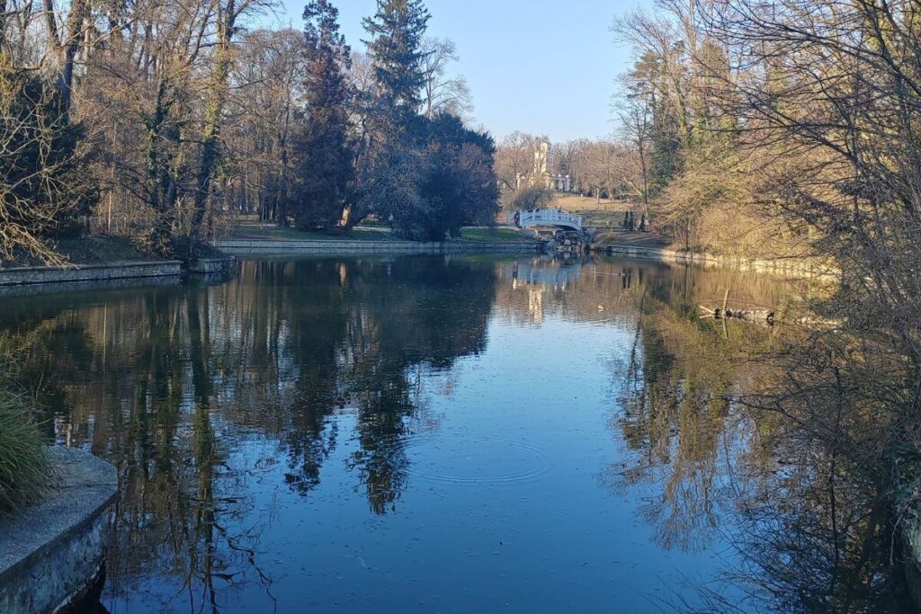 cenic view of the lake at Park Maksimir in Zagreb with the white Echo Pavilion building and stone bridge surrounded by forest.