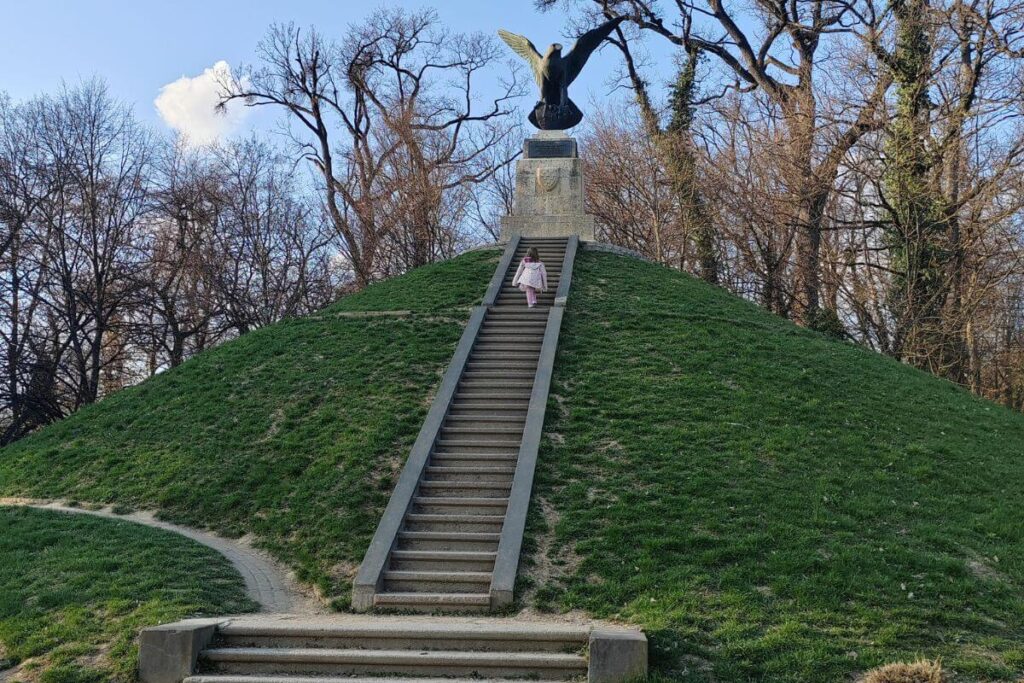 A child walking up a long flight of stone stairs leading to the top of the grassy Mogila mound.