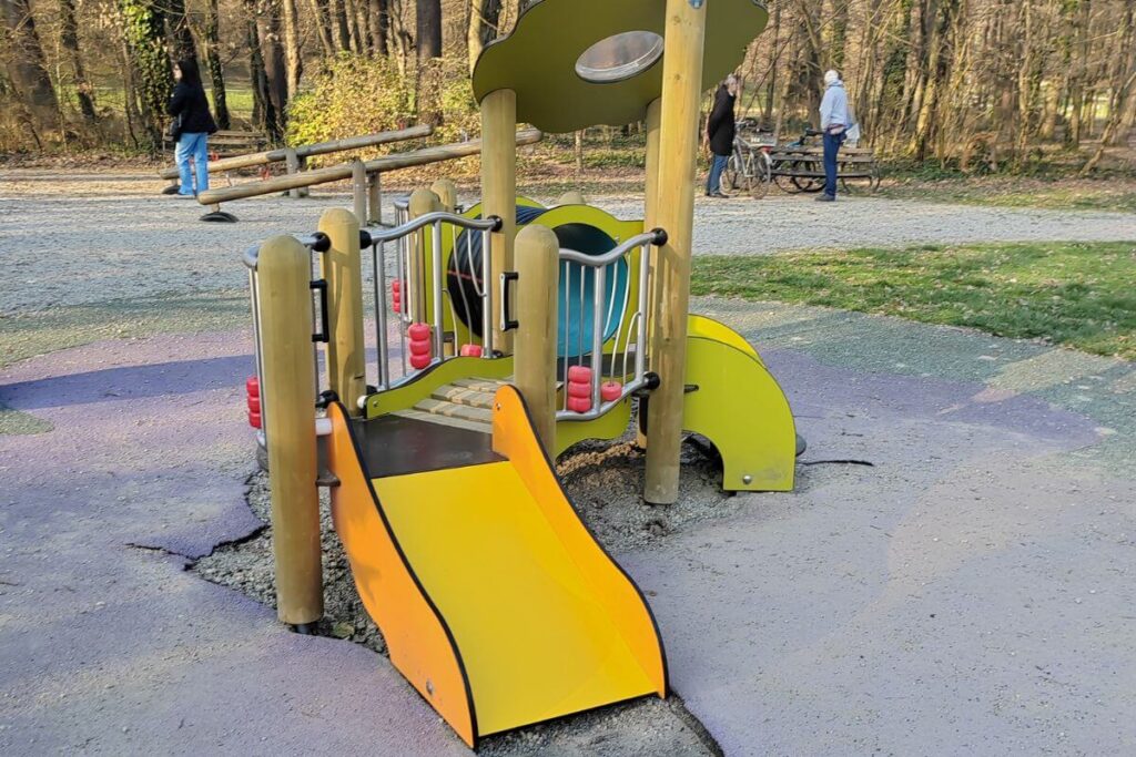 A colorful plastic and wood play structure with a yellow slide for toddlers in a park setting.