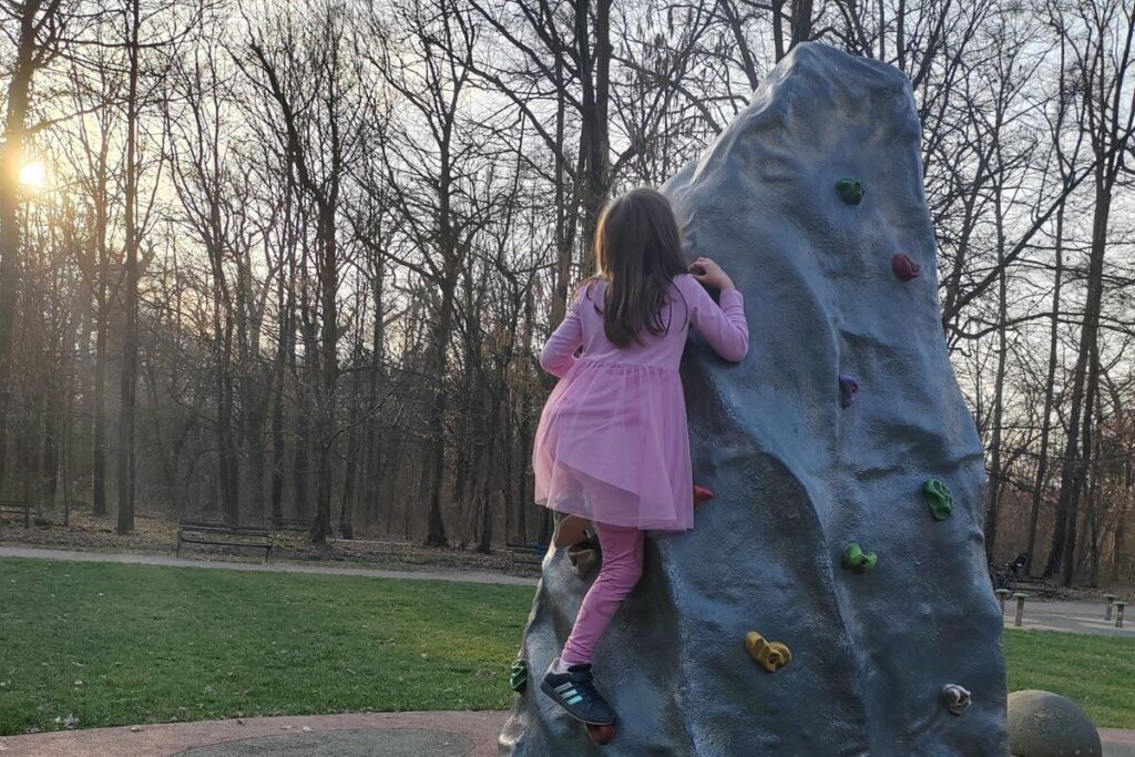 A young girl climbing an outdoor artificial rock wall at a playground in Maksimir Park.