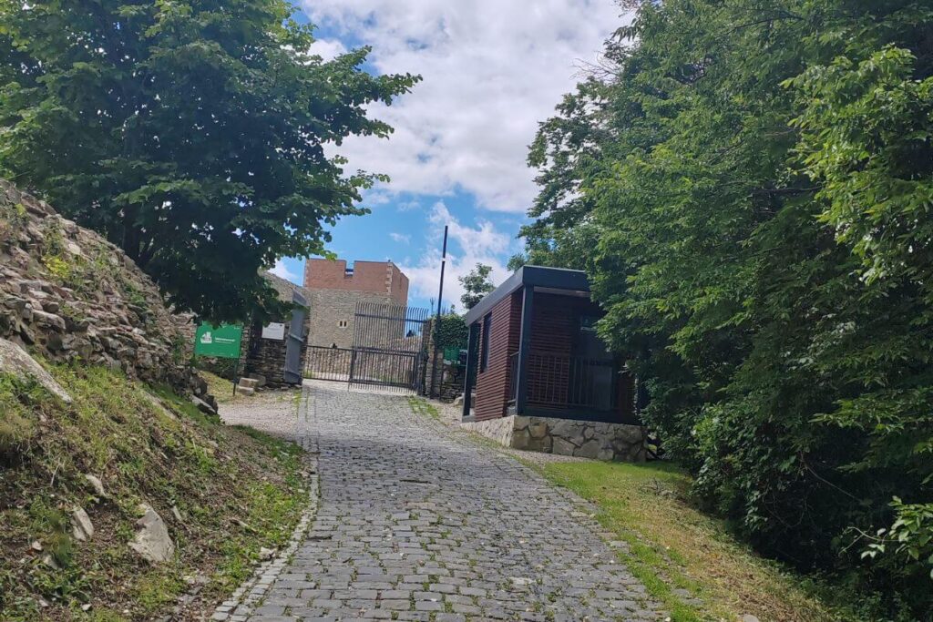 A paved stone incline leading up to the main security gate and modern visitor entrance building at Medvedgrad fortress.