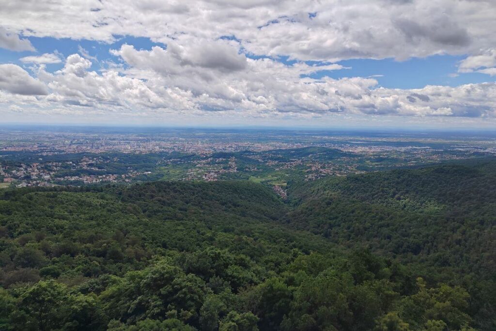 A wide panoramic view of the city of Zagreb stretching out to the horizon, viewed from high up on the green slopes of Medvednica mountain.
