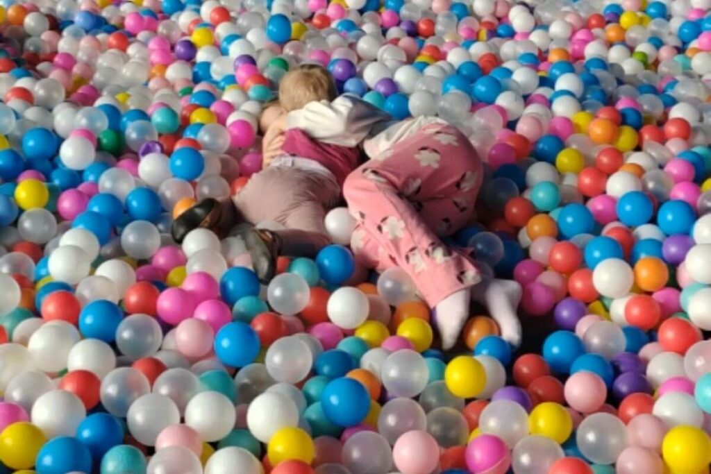 Two young kids playing and buried together inside a massive, colorful ball pit filled with plastic balls.