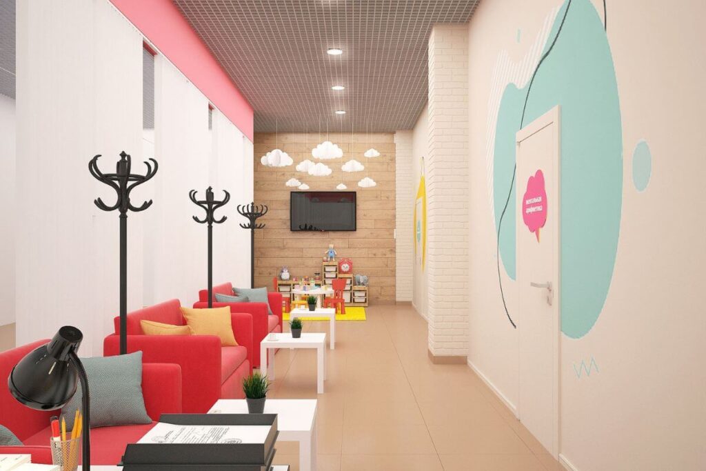 A modern, bright children's clinic waiting area with vibrant red couches, white tables, and a dedicated kids' play corner in the background.