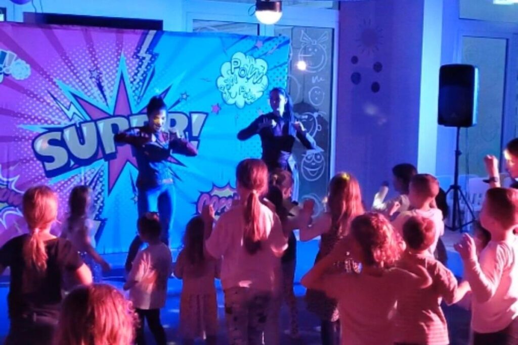 Children dancing in front of a colorful "SUPER!" comic book backdrop during the evening mini disco at Family Hotel Lišanj.