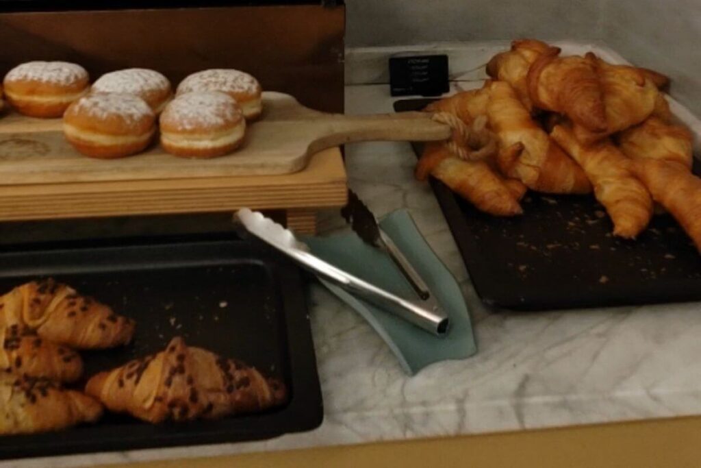 A buffet spread at Hotel Lišanj featuring fresh croissants, chocolate croissants, and powdered donuts on wooden platters.