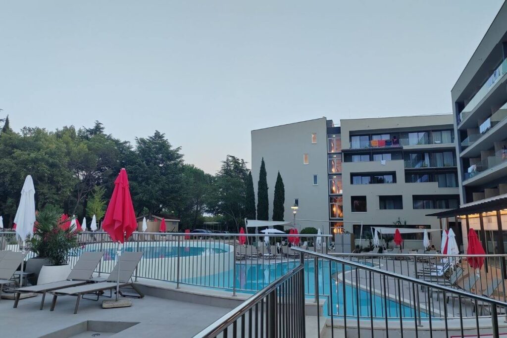 Outdoor swimming pool deck with loungers, pink sun umbrellas, and modern hotel buildings at Hotel Garden Istra Plava Laguna.