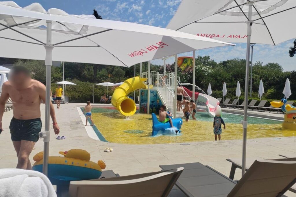 Children playing near a bright yellow spiral water slide in a shallow kids pool at Hotel Garden Istra Plava Laguna.