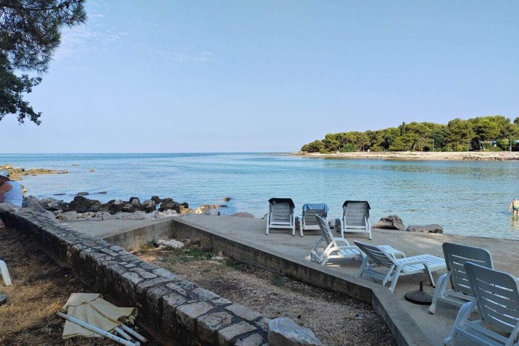 Paved coastal sunbathing deck with loungers overlooking a calm turquoise sea bay near Hotel Garden Istra Plava Laguna.