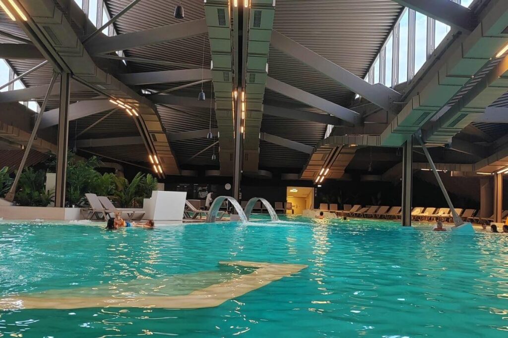 Spacious indoor thermal pool complex with lap lanes and rows of lounge chairs.