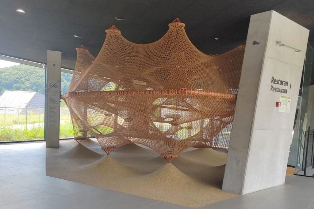 A large, woven rope net climbing structure for kids near the restaurant and entrance area at Terme Tuhelj.