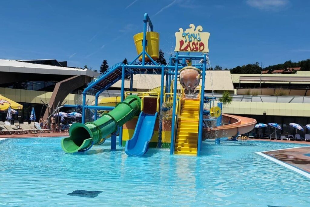 Bright yellow and green Tuhi Land water castle structure with slides and a splash bucket in an outdoor pool.