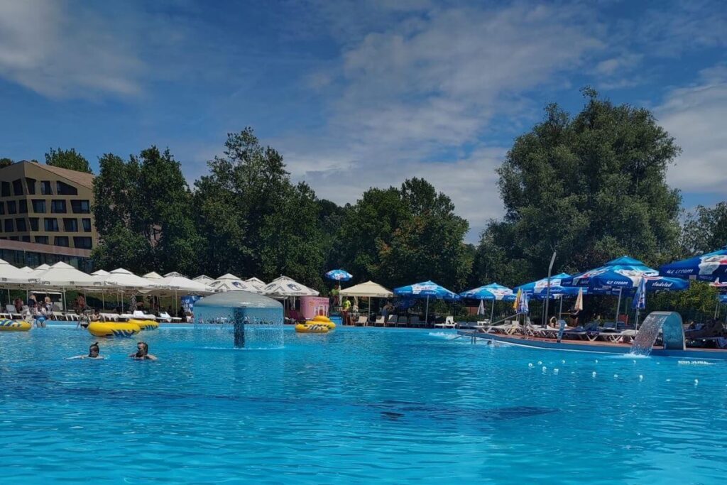 Large outdoor wellness pool with water fountains, surrounded by umbrellas and sunbeds at Terme Tuhelj.
