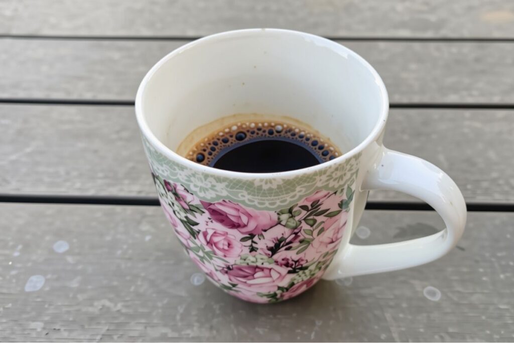 A floral ceramic mug filled with black coffee sitting on a wooden terrace table in Croatia