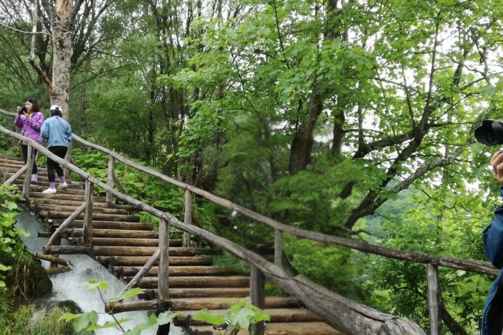Visitors walking up wooden stairs along the boardwalk trail beside a rushing waterfall at Plitvice Lakes National Park